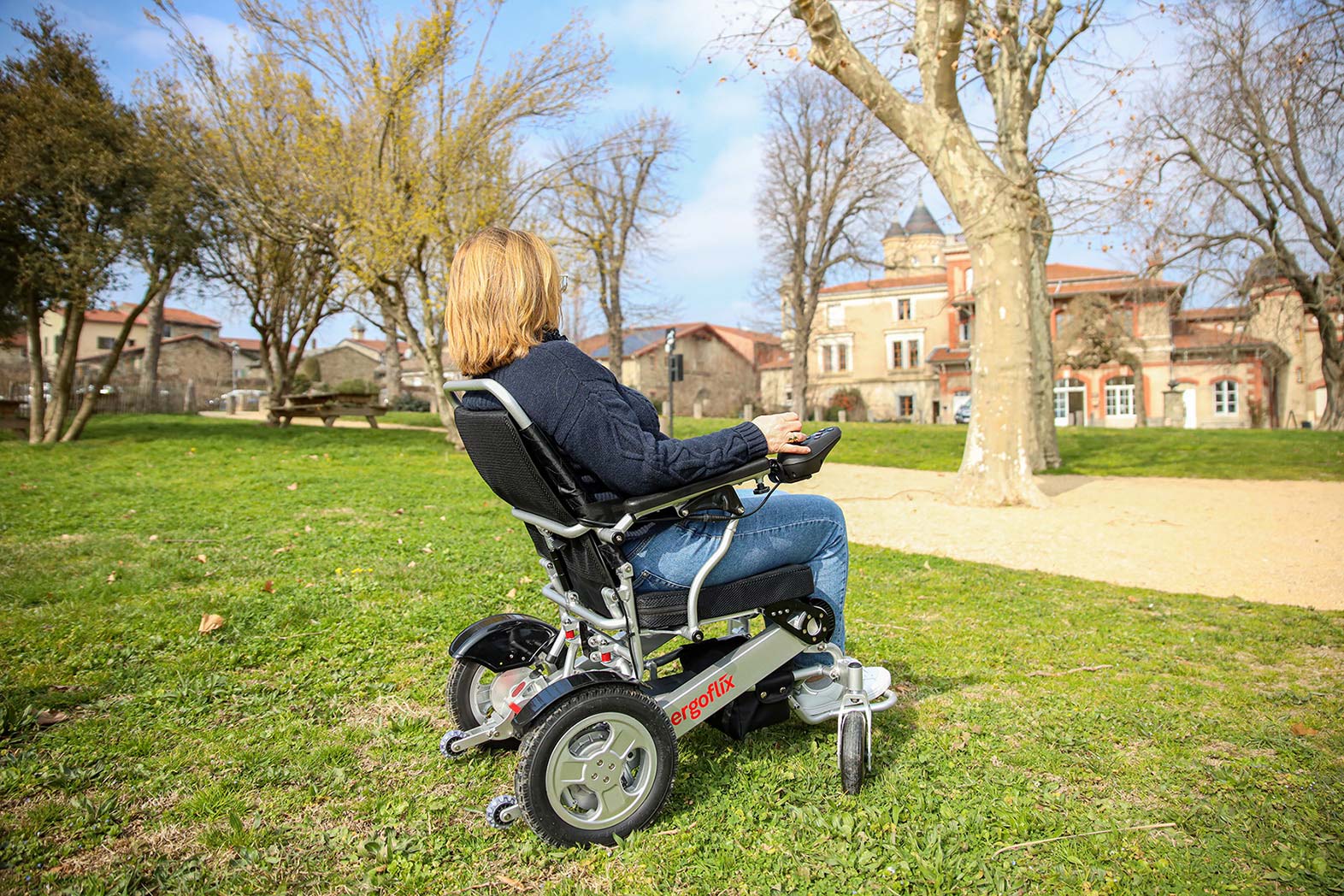 Fauteuil roulant électrique avec dossier inclinable Ergoflix L-Back déplié, utilisé par une personne en situation de mobilité réduite sur une pelouse dans un parc